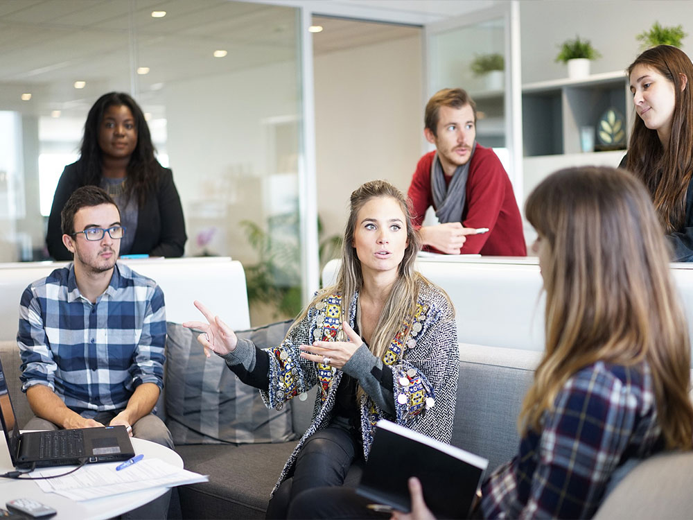 Group of people sitting in a meeting in an office holding computers and notpads